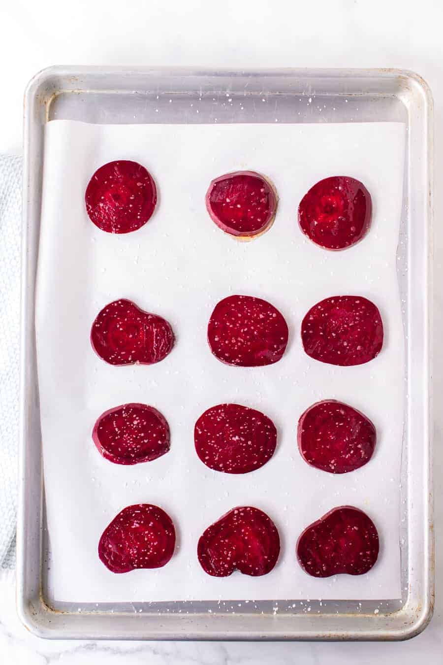 top view of a baking sheet with slices of round and thin raw beets ready to be baked.