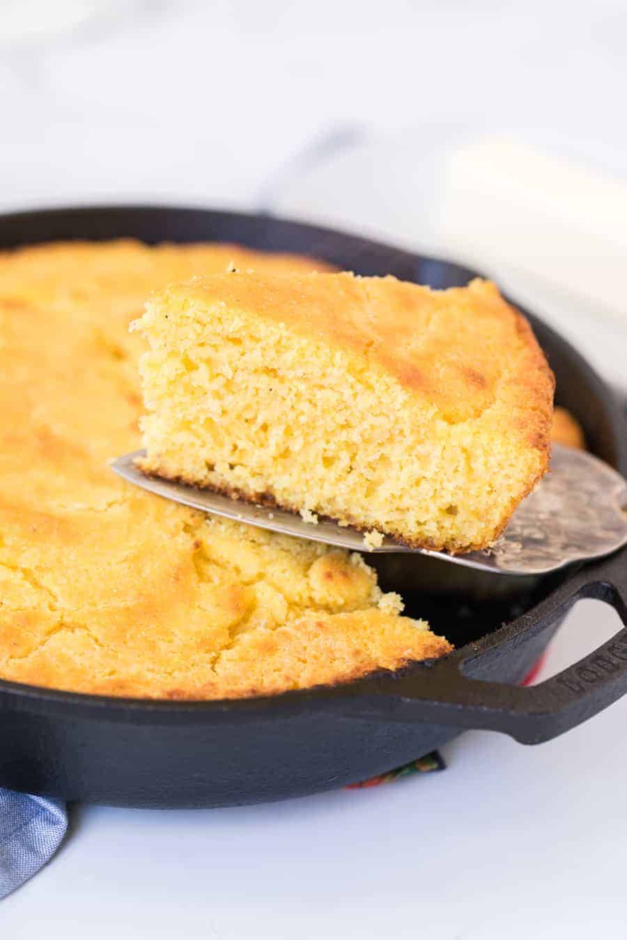 cornbread baked in a cast iron skillet and a spatula scooping out one perfect triangle slice.