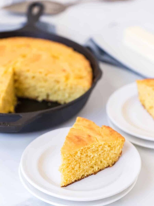 cornbread baked in a cast iron skillet in the background then triangle pieces have been served on white plates