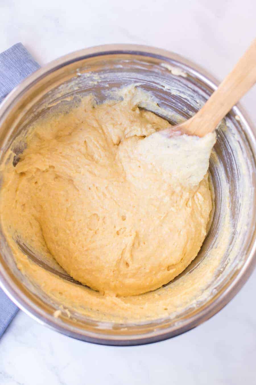 corn bread dough with a wooden spoon in a silver mixing bowl.