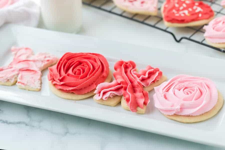 a plate of valentines day sugar cookie with piped pink and red roses as the O's and Red and Pink piping as X's designed in the frosting to form "XOXO" cookies laid out on a plate.