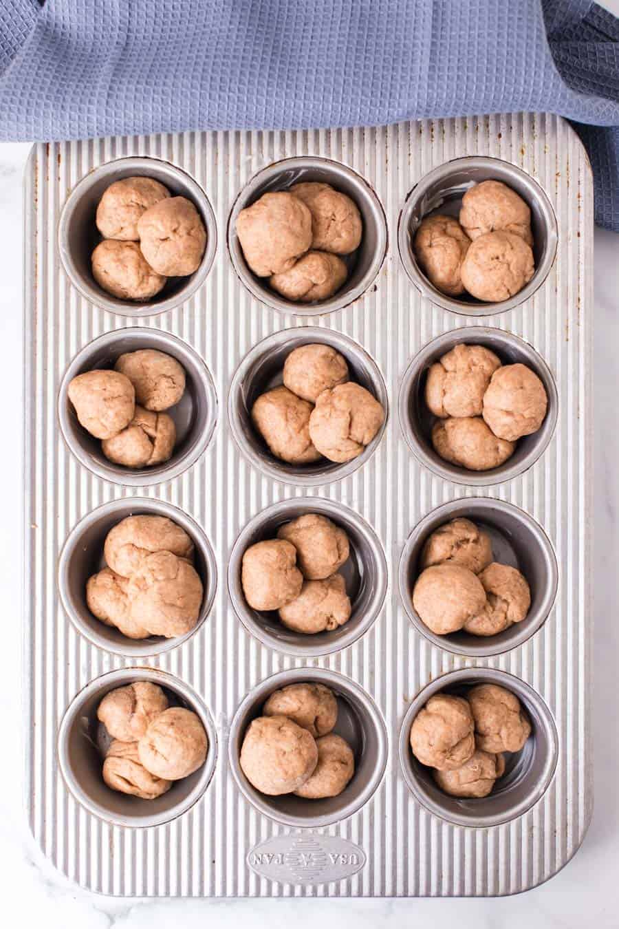 top view of raw whole wheat clover roll dough in a muffin tin.