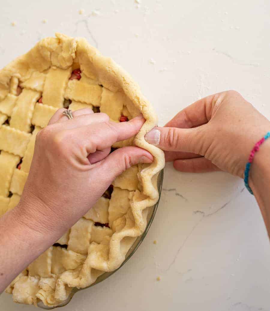 Hands pinching the outside dough of pie crust together. 