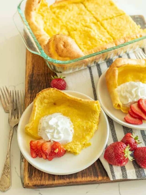 german pancakes cut and served on white plate with strawberries and whipped cream on top