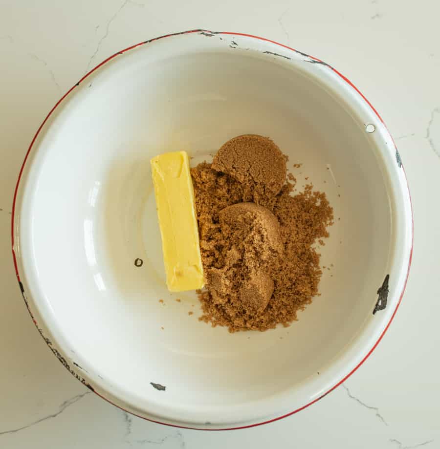 Butter and brown sugar in a white bowl with a red rim on a white marble counter. 