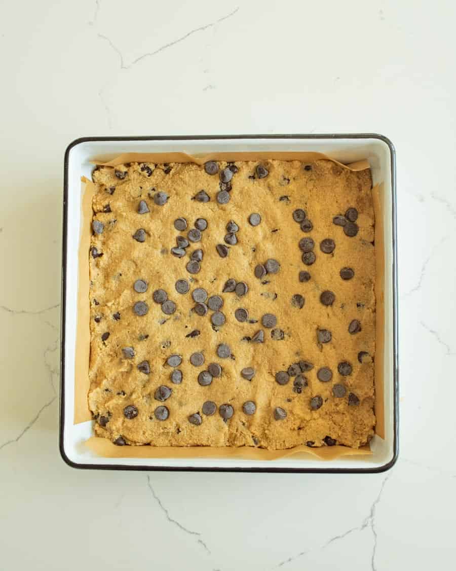 Almond flour cookie bar dough pressed in pan with chocolate chips on top. 