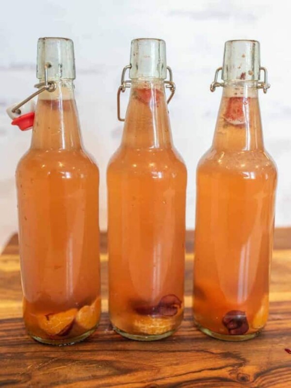 thee open wire lid carafe bottles of orange second ferment kombucha with oranges and cherries on bottom