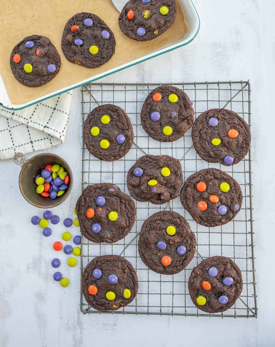 Halloween dark chocolate M&M cookies being transferred from baking sheet to cooling rack.