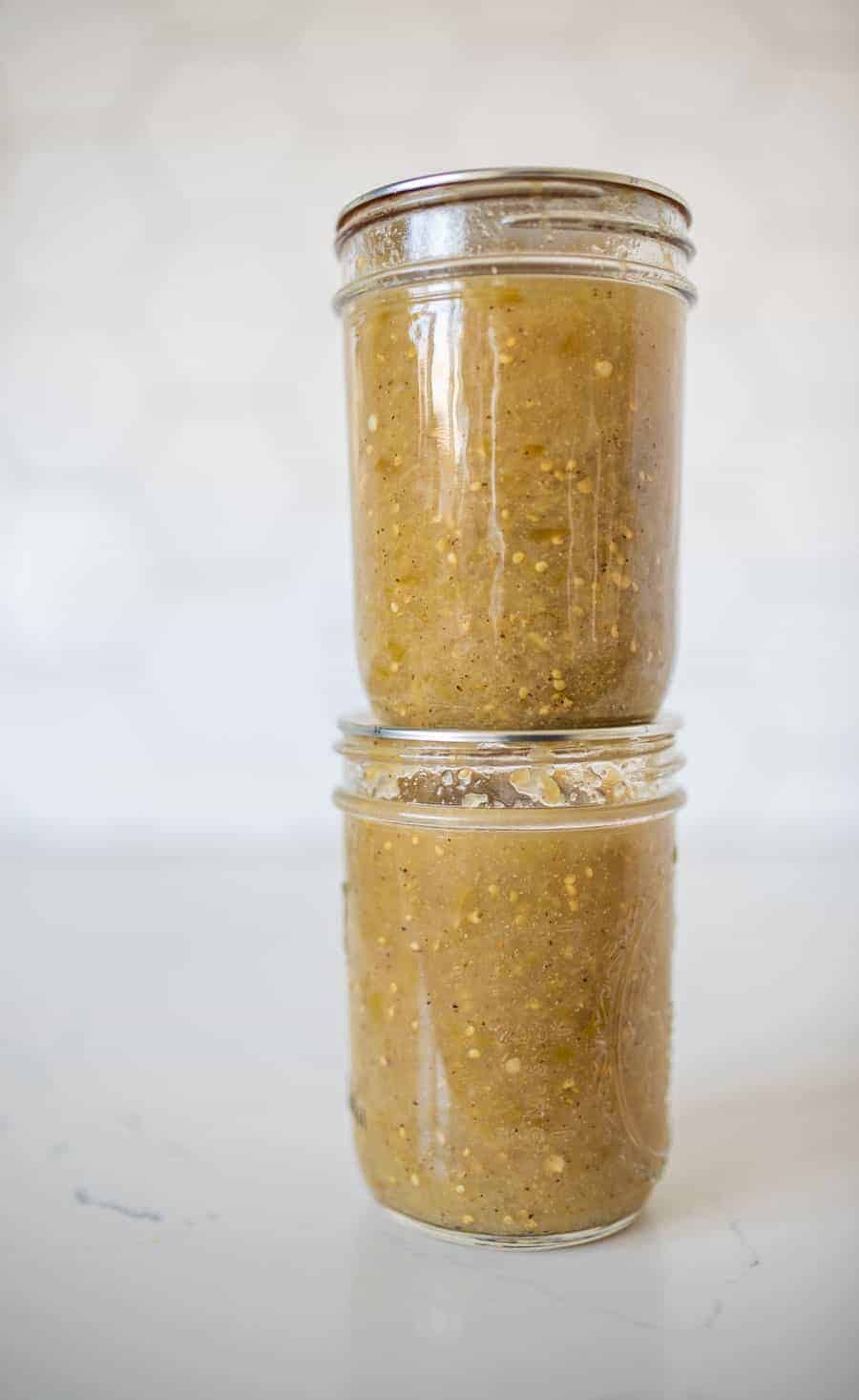 Two jars of tomatillo salsa stacked on a white counter. 