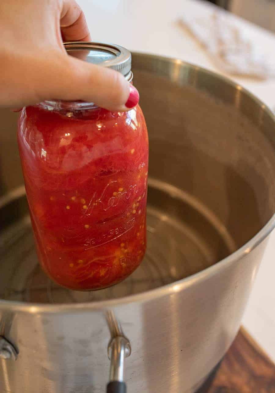 A woman's hand putting a jar of tomatoes into water bath canner. 