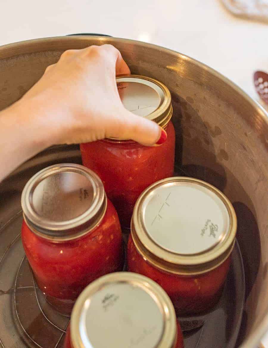 A woman's hand adding a fourth jar into a water bath canner. 