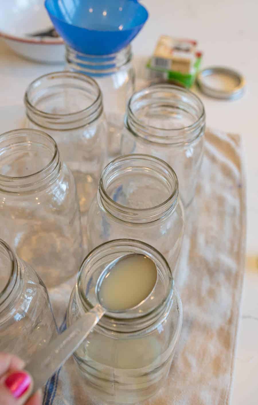 A measuring spoon adding lemon juice to a quart-sized Mason jar. 