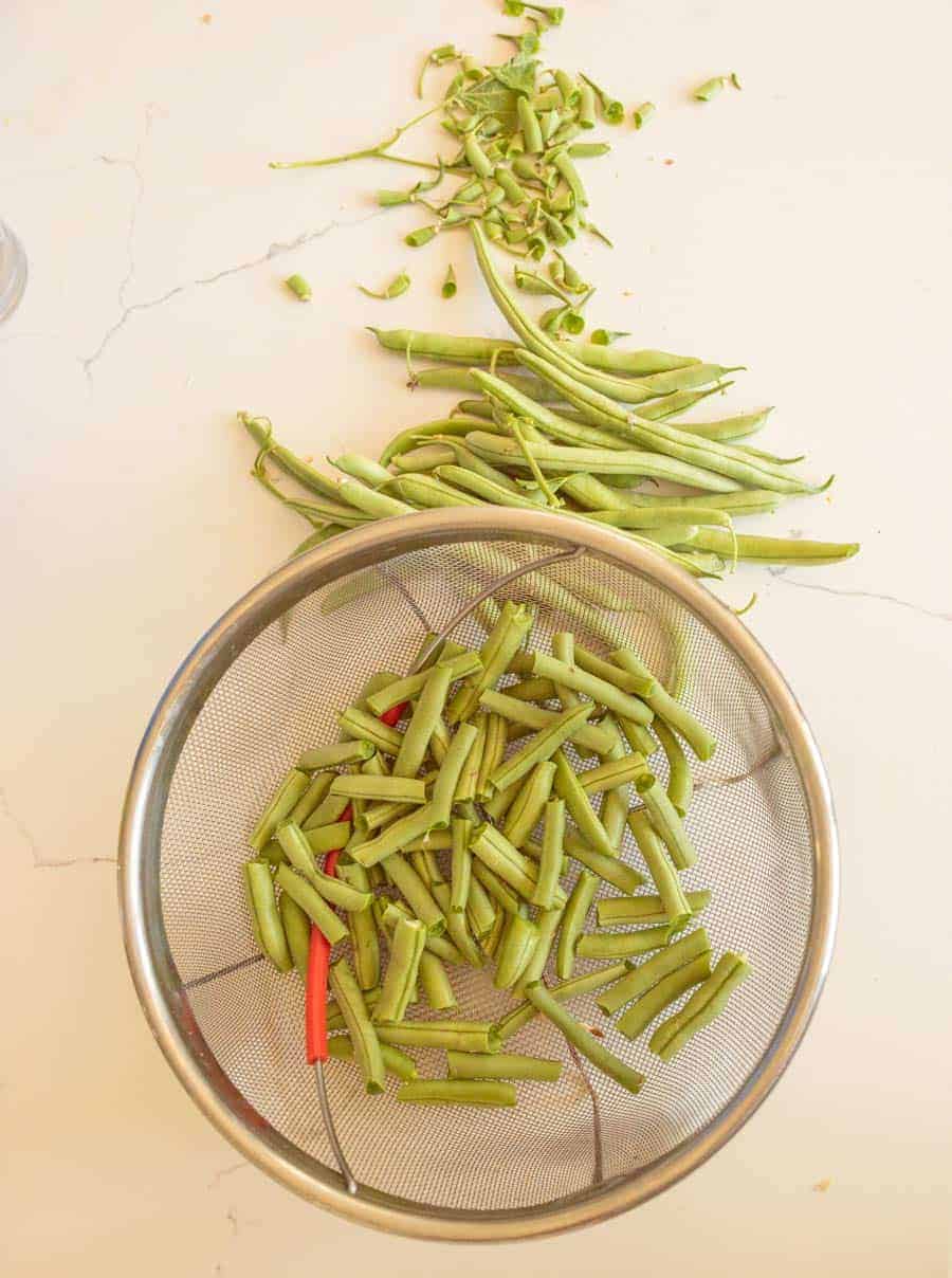 snapped green beans in strainer with un-snapped beans