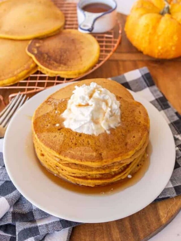 pile pf pumpkin pancakes on white plate with whipped cream