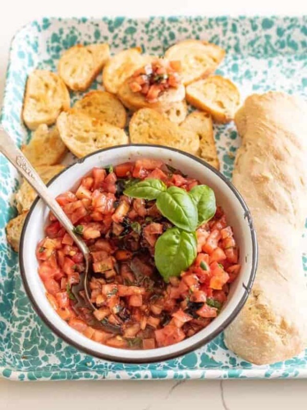 bowl of bruschetta garnished with fresh basil and a whole loaf then some of the crisped bread peices