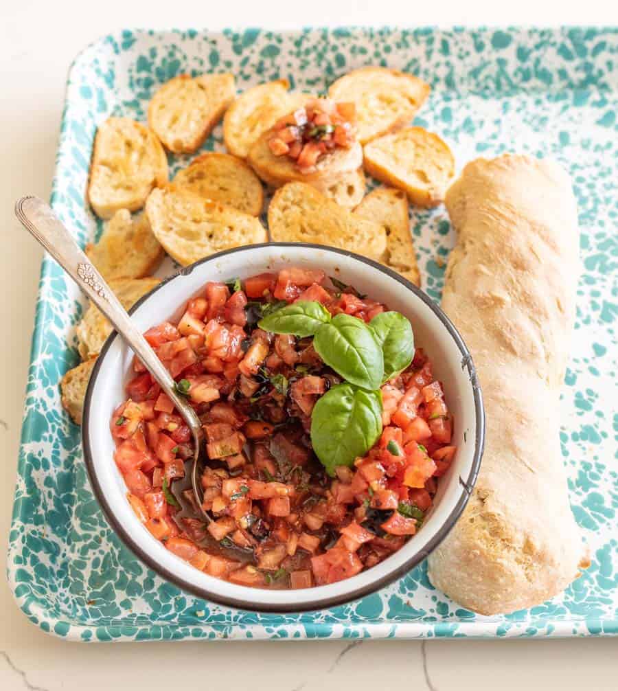 bowl of bruschetta garnished with fresh basil and a whole loaf then some of the crisped bread pieces.