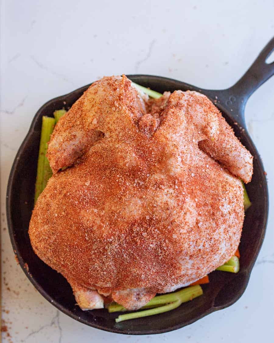 A whole raw chicken in cast iron skillet ready to be roasted in the oven. 