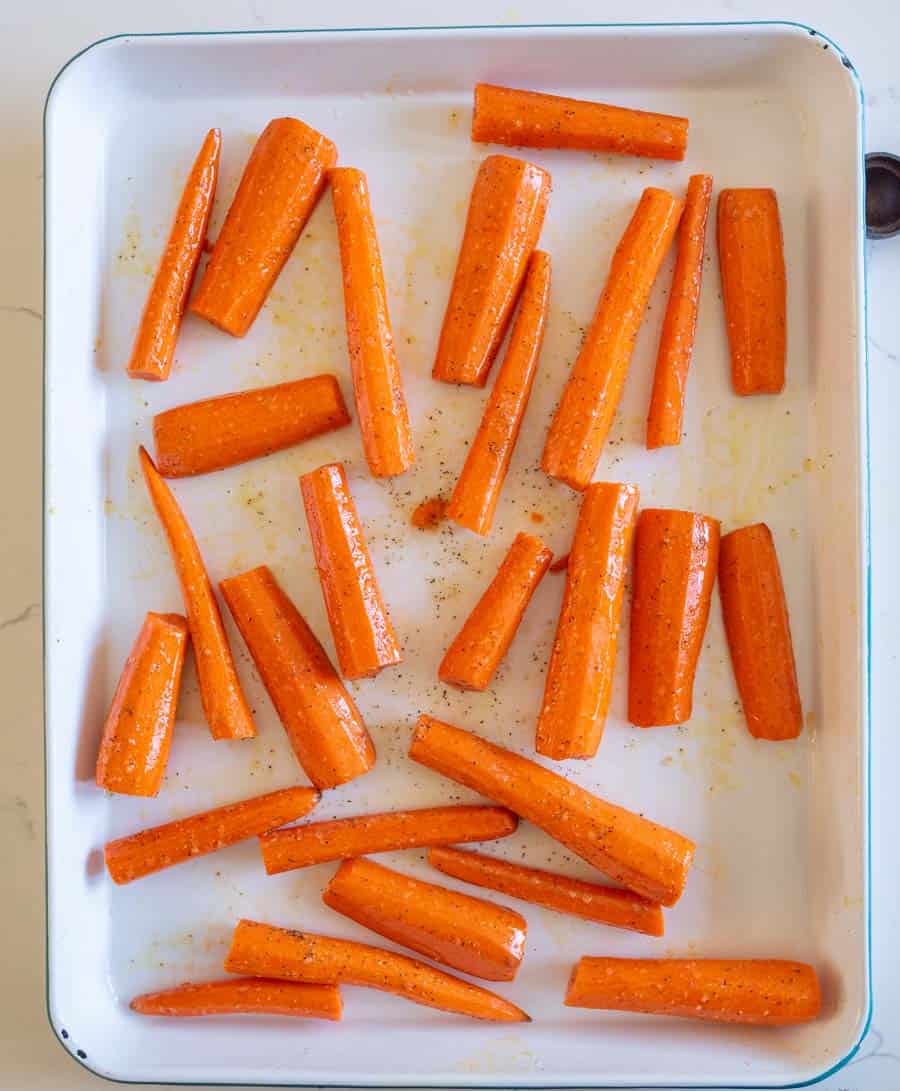 Carrots on a white enamel baking pan before roasting.