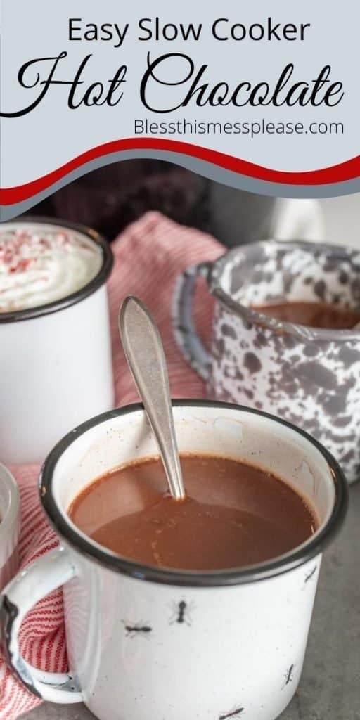 Picture of a white mug of hot chocolate with a spoon in it and a few mugs in the background and the words "easy slow cooker hot chocolate" written at the top