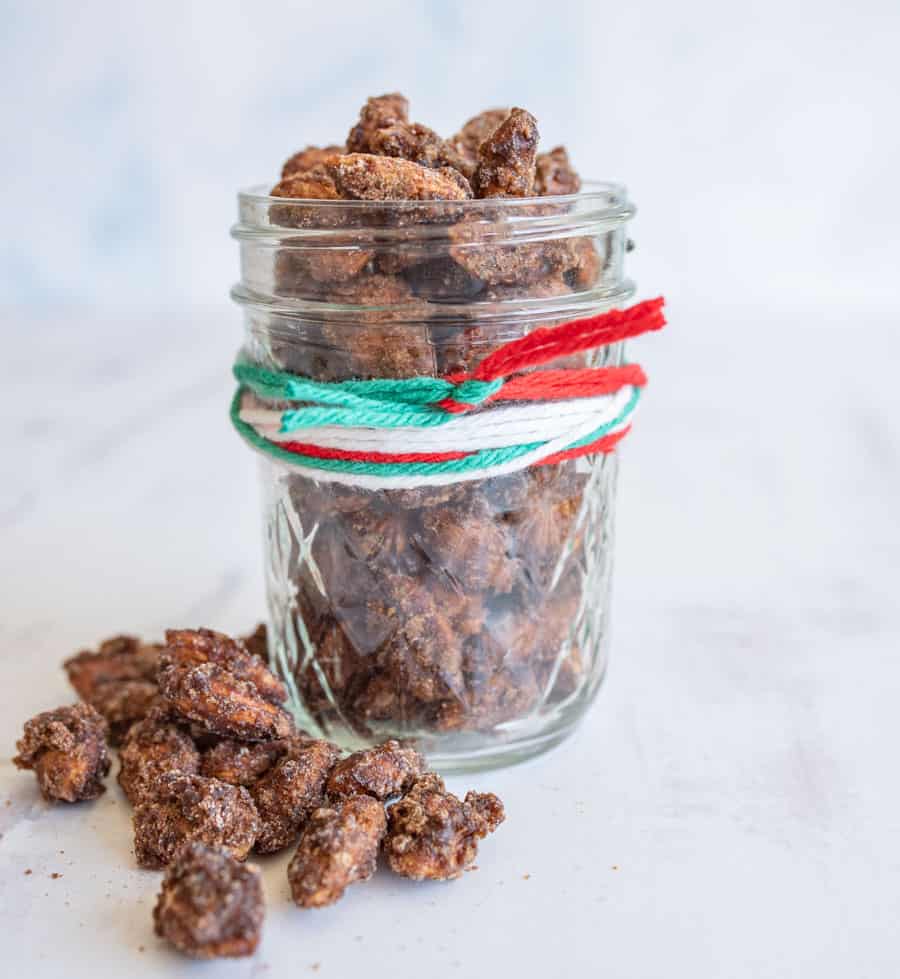 Cinnamon candied almonds in a glass pint-sized Mason jar that has green, red, and white yarn wrapped around it. 