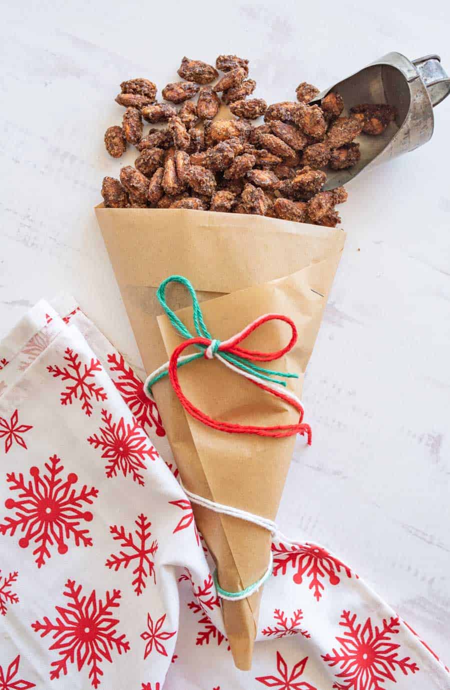 Top view of cinnamon candied almonds spilling out of a brown paper bag tied with green, red, and white yarn.