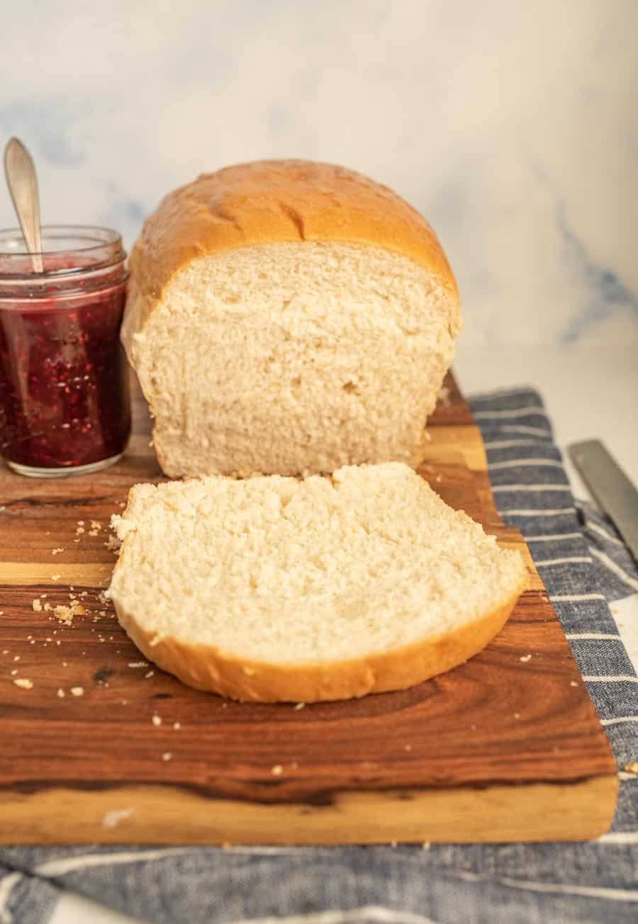 A slice cut from a loaf of white sandwich bread with a jar of jelly next to it.
