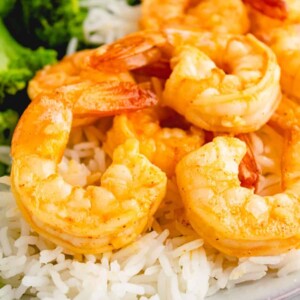 close up of dish with cooked garlic shrimp over white rice and broccoli to the side