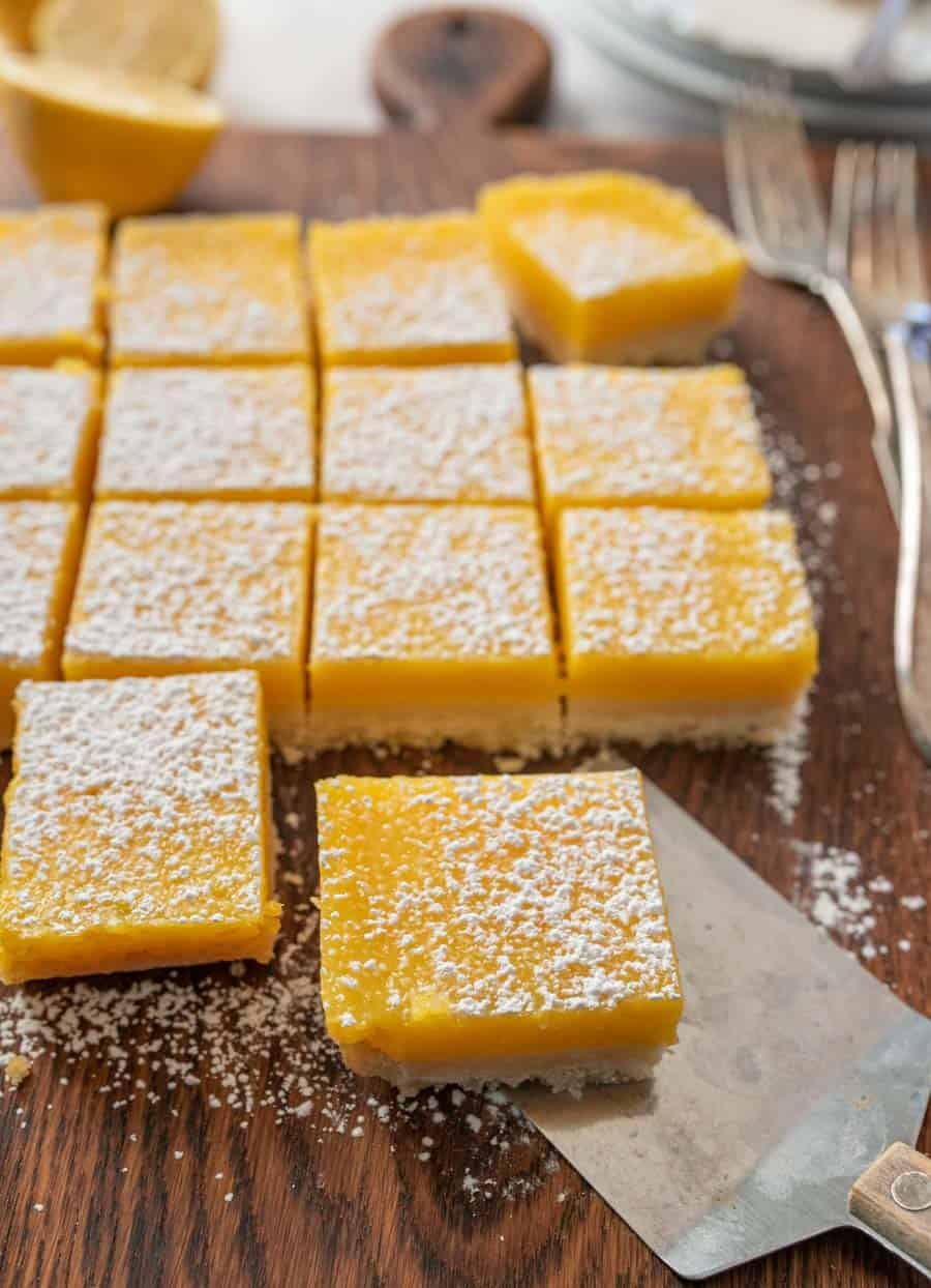 Lemon bars sprinkled with powdered sugar with one bar being removed by a thin metal spatula. 
