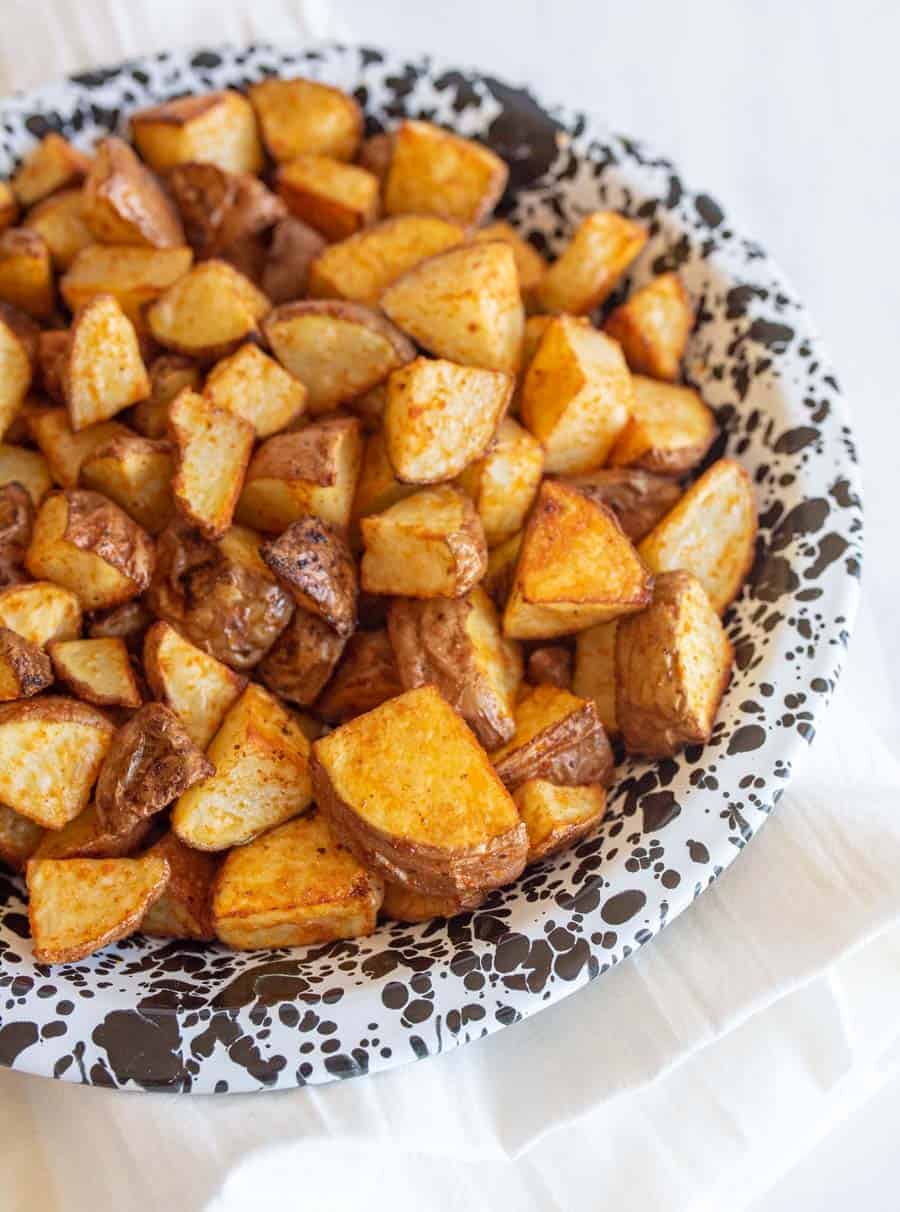 Roasted red potatoes in a white bowl with black speckles.