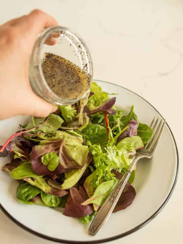 hand pouring salad dressing over a plate of salad featuring easy salad dressing recipes.