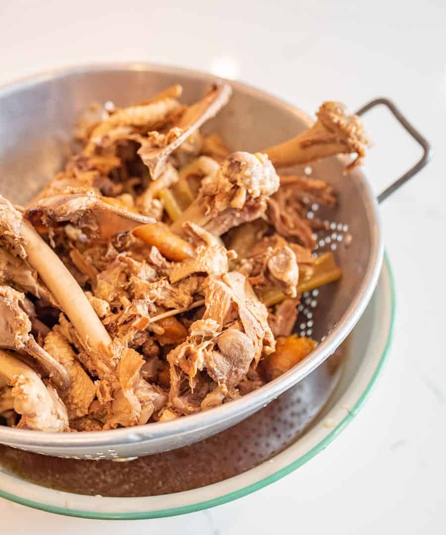 Picture of chicken and bones in a colander over a bowl of broth
