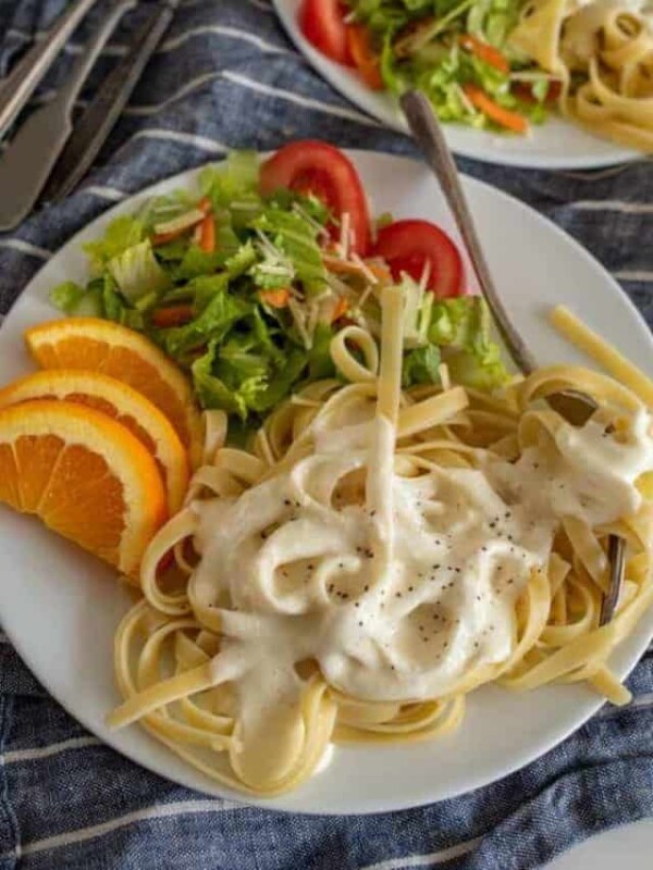 up close picture of a plate of alfredo pasta with salad and orange slices