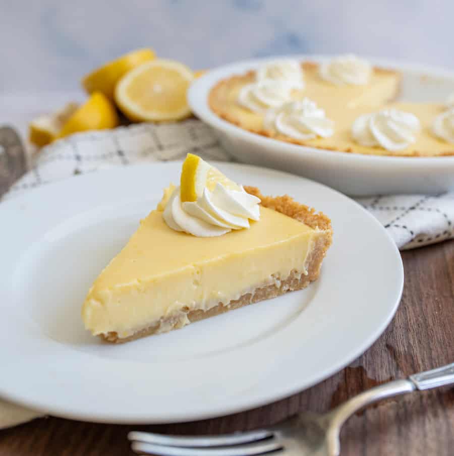 close up of a slice of lemon pie with the pie in the background