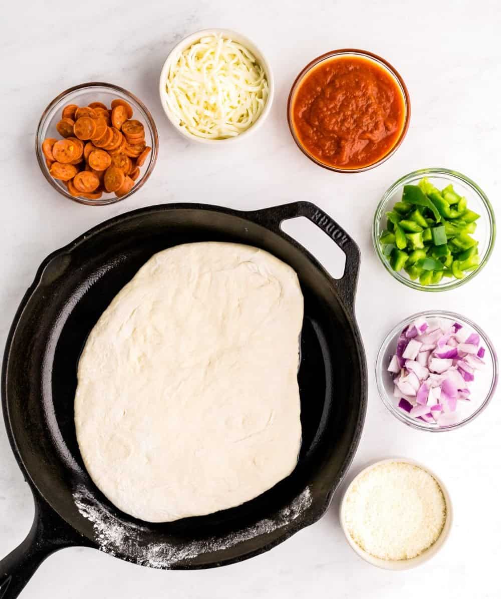 A top view of bowls of ingredients and dough in skillet for pizza. 