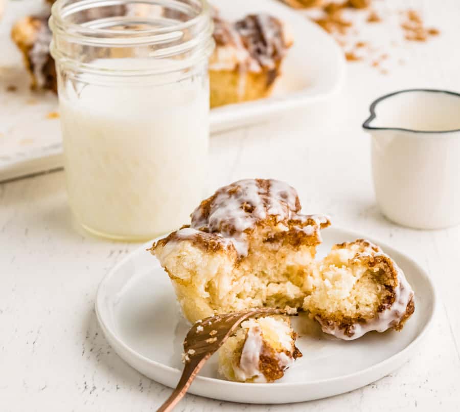 Monkey bread muffin cut in half on plate with a fork and a cup of milk in background. 
