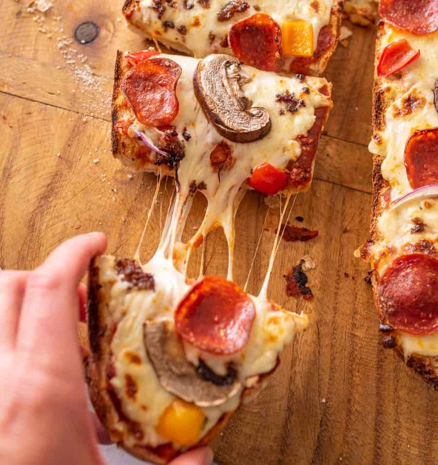 picture of a hand picking up a slice of French bread pizza
