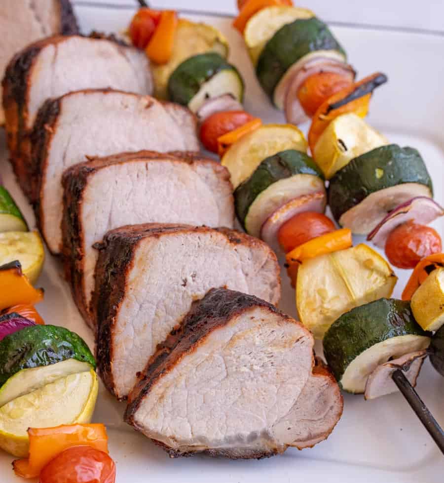 slices of grilled pork loin with vegetable kabobs next to them