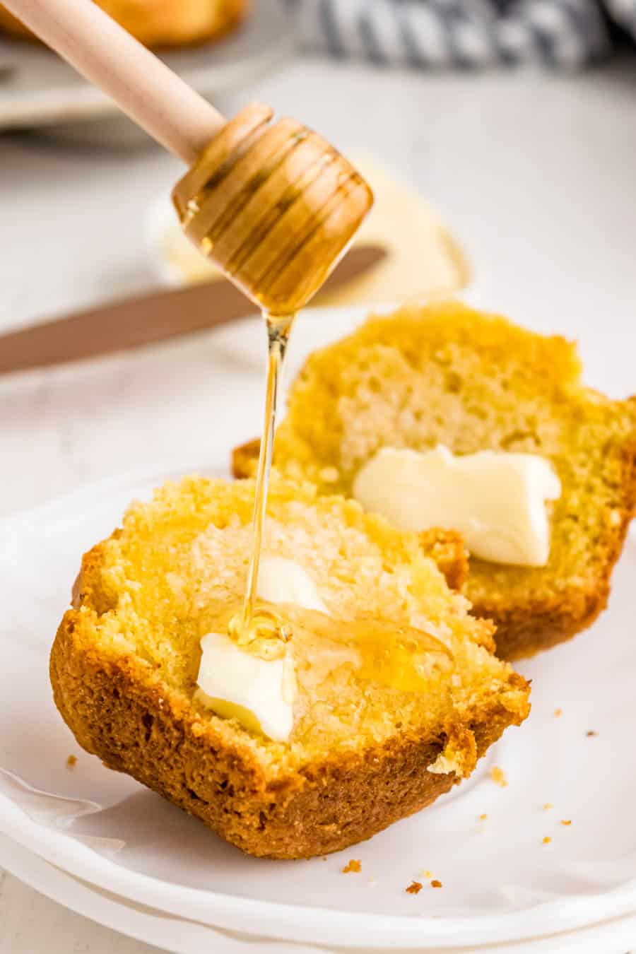 homemade cornbread muffins on a white plate with honey on top.