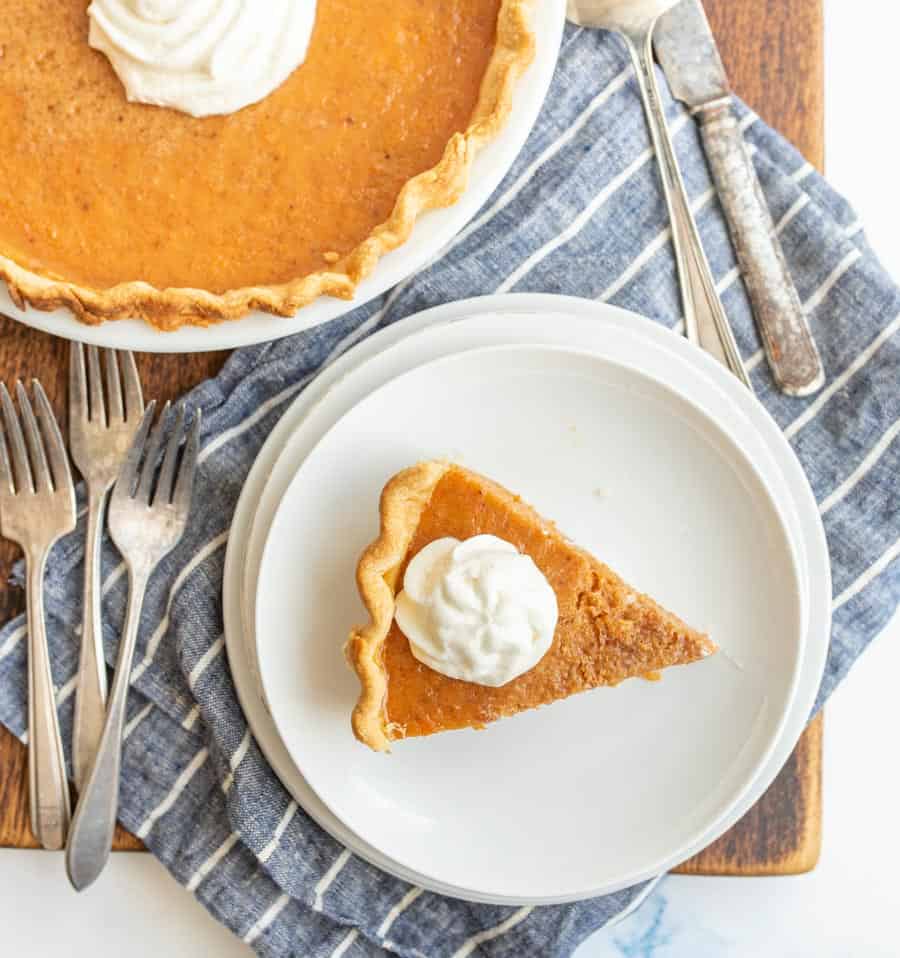 top view of a slice of sweet potato pie with whipped cream next to a sweet potato pie