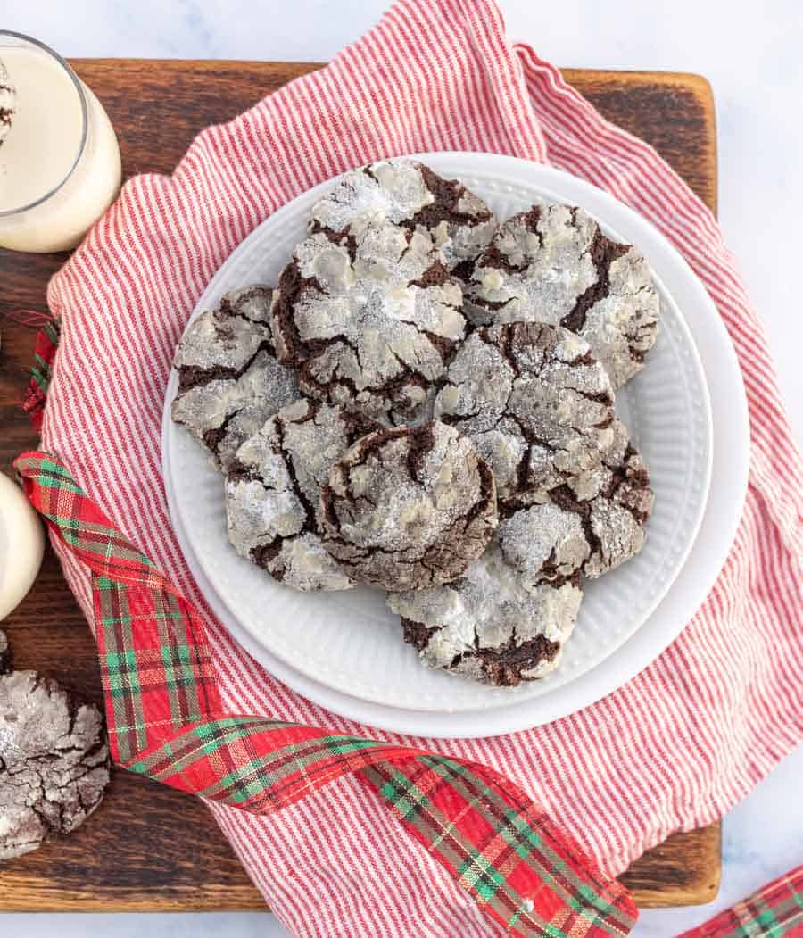 Top view of a christmas rag with white plate and cracked cookies that are nearly white on top but the cracks reveals dark chocolaty lines. 