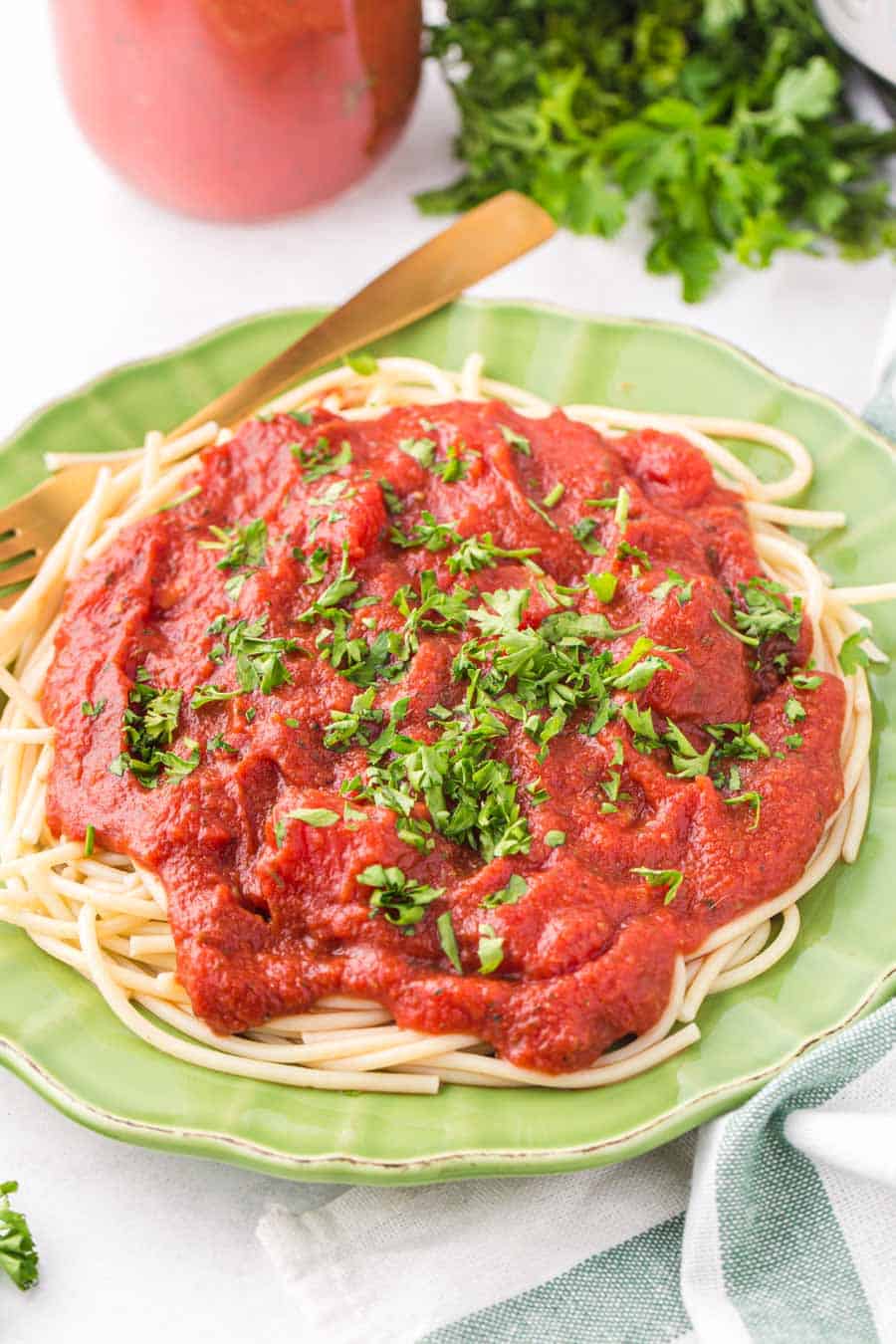 jade green plate with a heaping amount of sauce and fresh parsley over spaghetti pasta