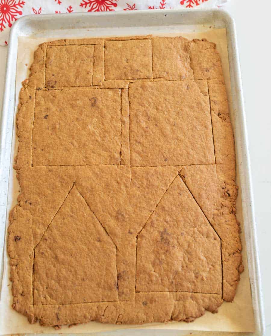 cutting out of a sheet pan of gingerbread cookie house shaped pieces