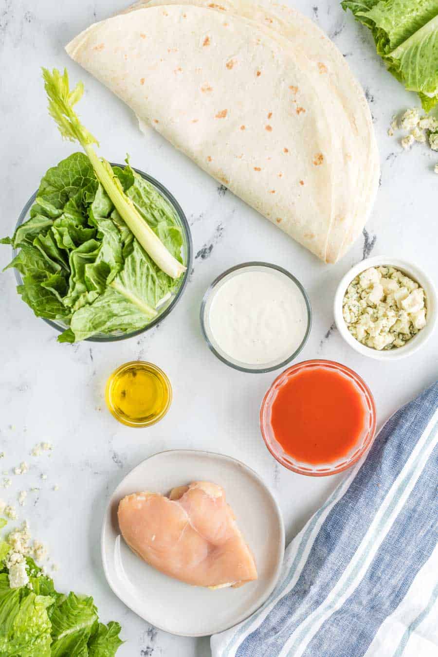 Top View of raw ingredients for buffalo chicken wrap with flour tortilla - lettuce - oil - spices - and dressing. 