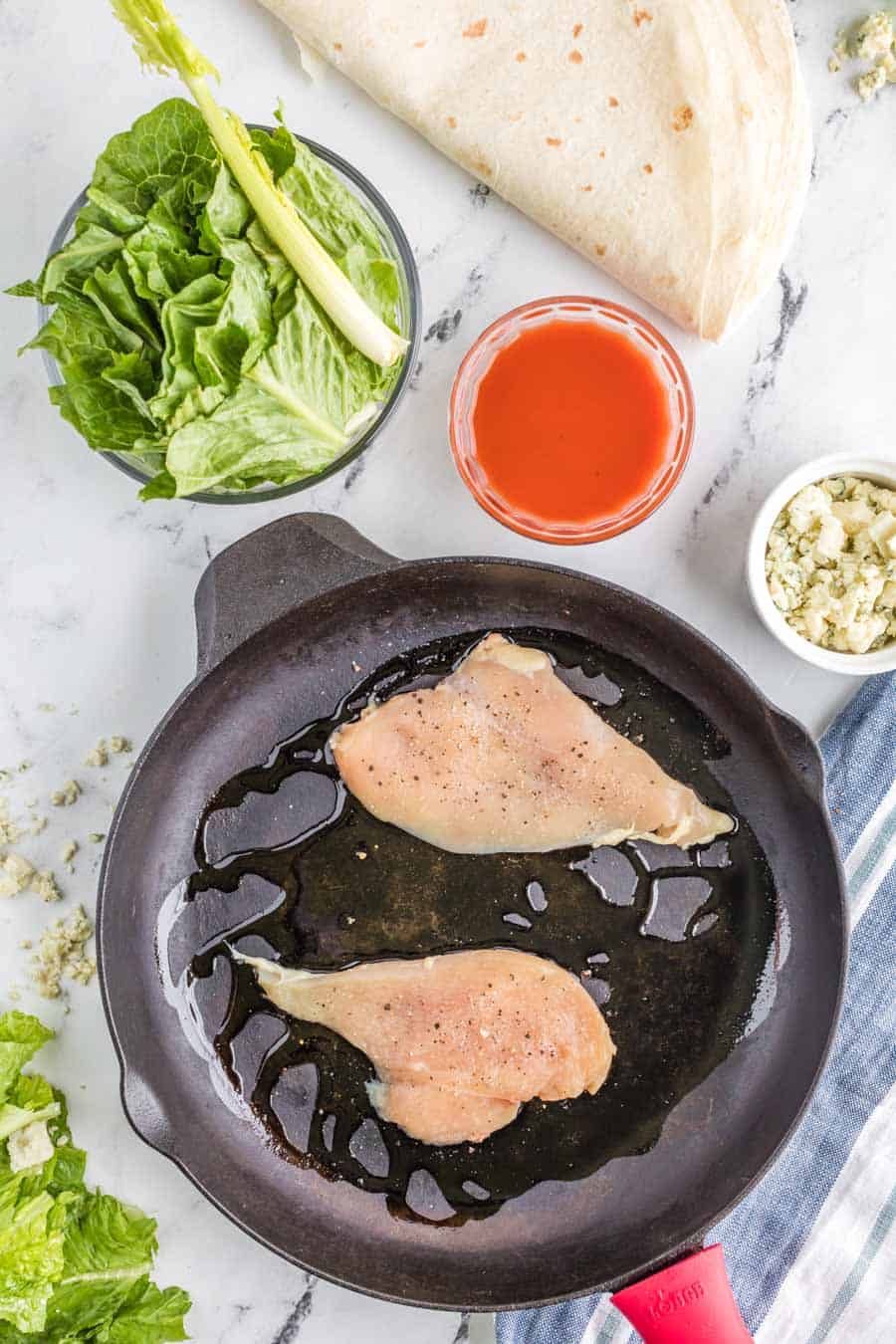 raw chicken with oil in a pan with other raw wrap ingredients around it