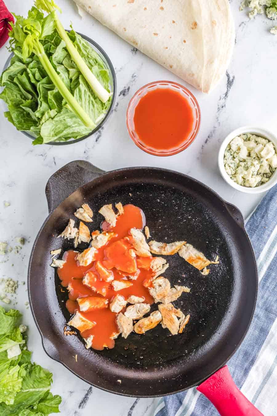 cooked chicken with sauce in a pan with other raw wrap ingredients around it