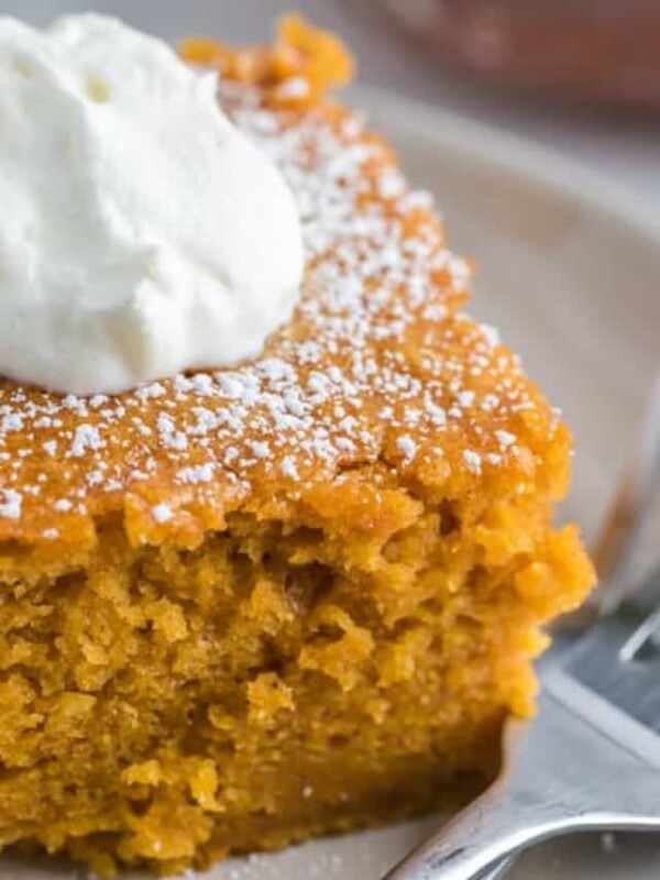 close up view of a square serving of extra thick pumpkin cake on a white plate with a dollop of cream with silver forks