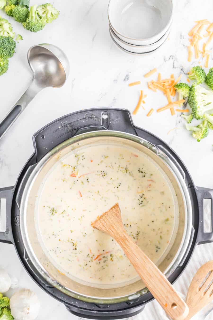 top view of an instant pot as cream is then added to the the broccoli soup stock and stirred with a wooden spoon