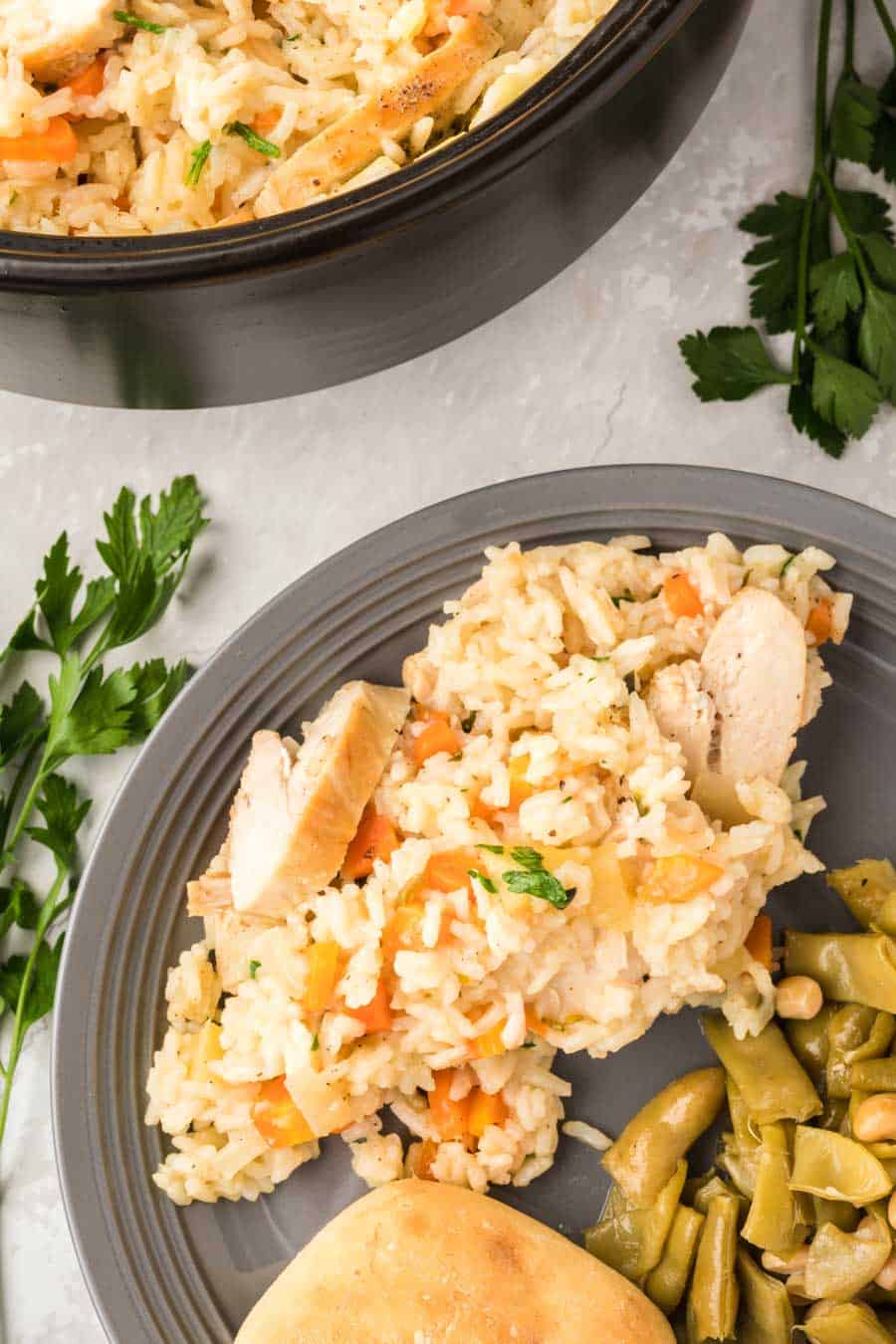 Close up of a grey plate and a savory rice dish with seasonings and chicken folded in, a biscuit and green beans to complete the dinner. 