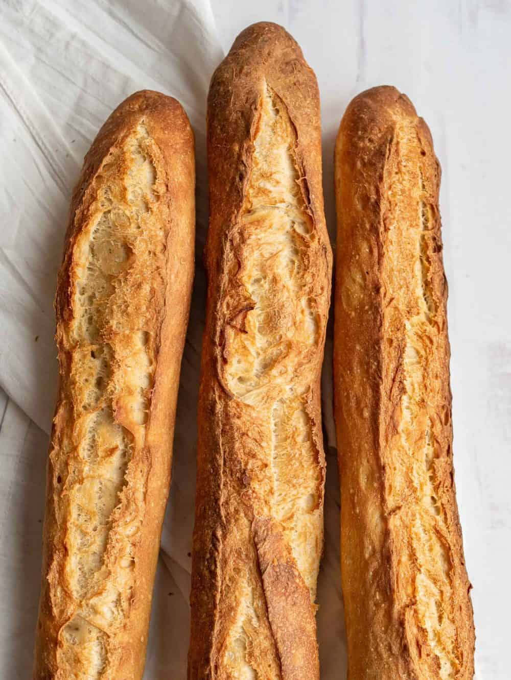 Three traditional baguettes on light wood. Plain, whole wheat and