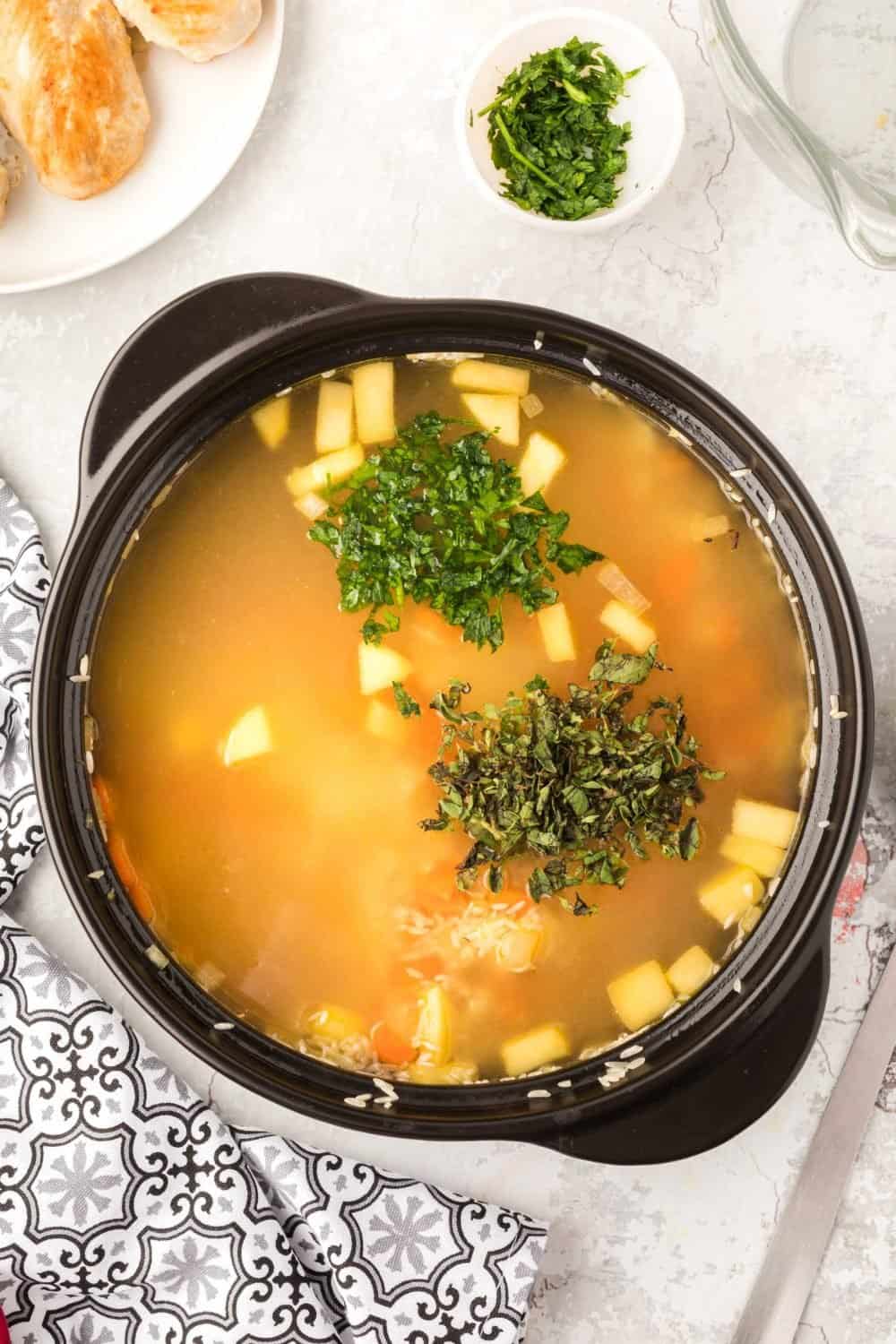 iron bowl with broth and vegetable rising to the top with green fresh herbs on top